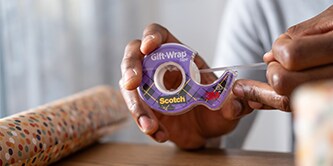 Mężczyzna zapakowujący prezent przy użyciu Scotch® Gift-Wrap Taśmy do pakowania prezentów
